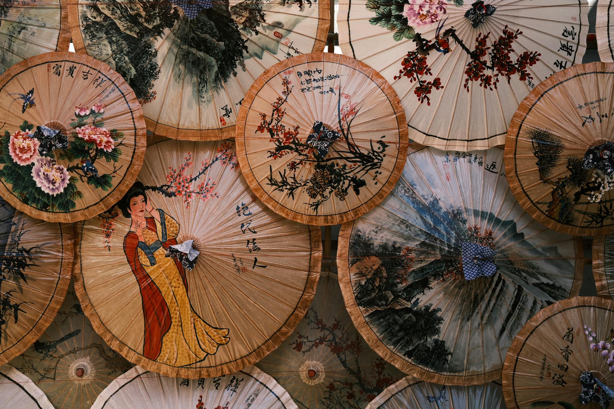 Close-up view of intricately decorated traditional Asian paper umbrellas with floral and figure designs.