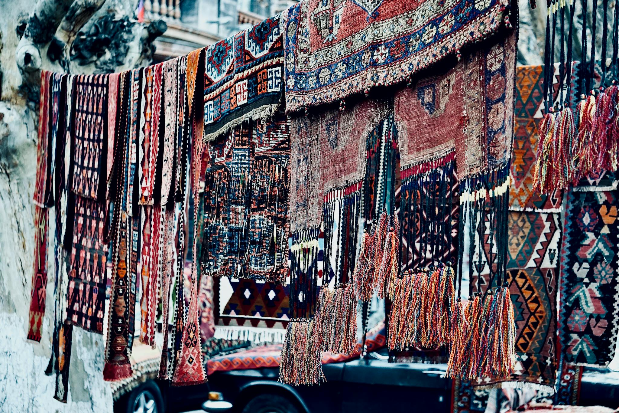 Colorful handmade rugs with intricate patterns displayed outdoors for sale.